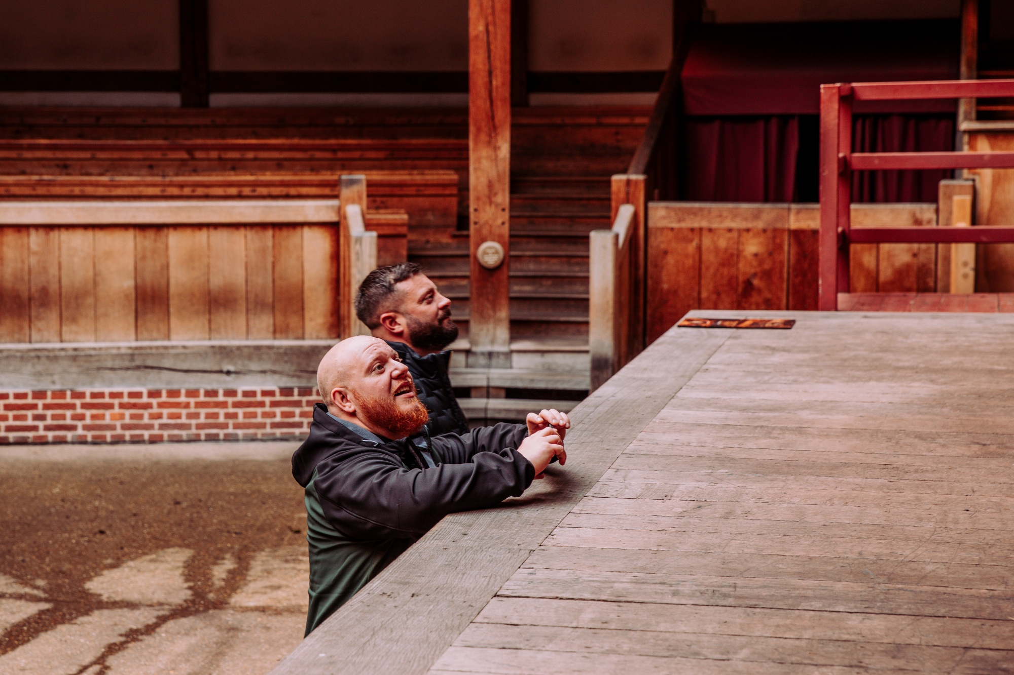 Two men in the Globe Theatre looking up at the stage from the stalls.