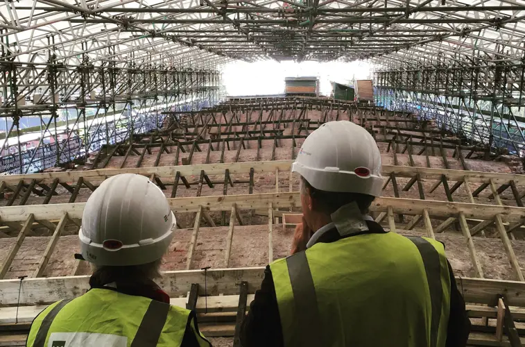 Two people overlooking repairs to an historic factory roof, surrounded by scaffolding.